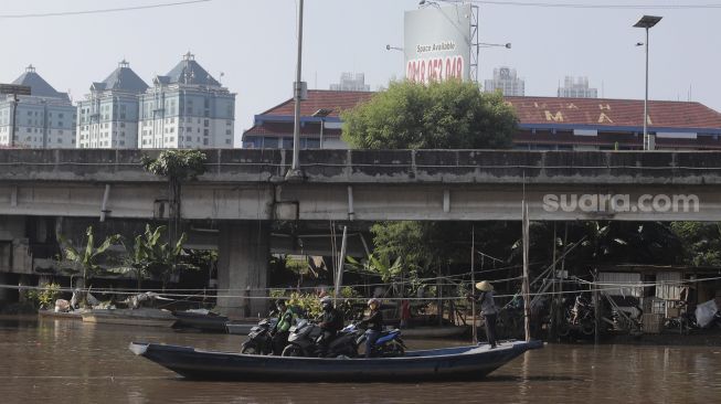 Sejumlah pengendara sepeda motor menggunakan perahu eretan untuk menyeberangi Kali Cagak, Jakarta Utara, Selasa (25/5/2021). [Suara.com/Angga Budhiyanto]