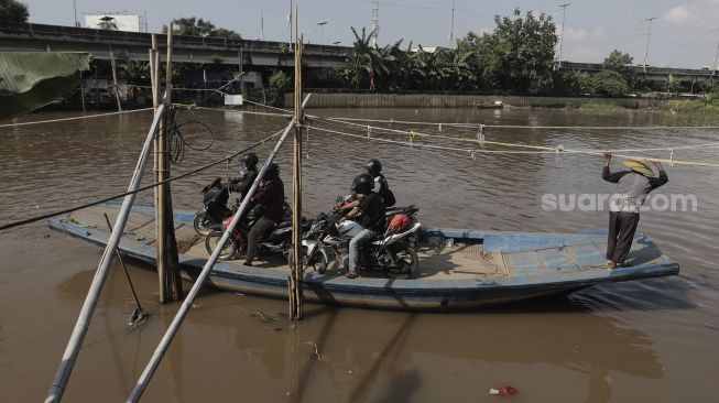 Sejumlah pengendara sepeda motor menggunakan perahu eretan untuk menyeberangi Kali Cagak, Jakarta Utara, Selasa (25/5/2021). [Suara.com/Angga Budhiyanto]