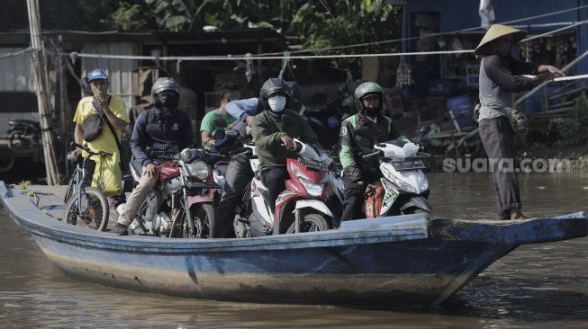 Sejumlah pengendara sepeda motor menggunakan perahu eretan untuk menyeberangi Kali Cagak, Jakarta Utara, Selasa (25/5/2021). [Suara.com/Angga Budhiyanto]