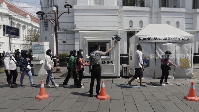 Petugas memeriksa suhu tubuh pengunjung yang akan memasuki kawasan Wisata Kota Tua, Jakarta, Rabu (26/5/2021). [Suara.com/Angga Budhiyanto]