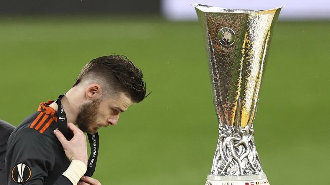 Kiper Manchester United David de Gea berjalan melewati trofi setelah kekalahan mereka dalam pertandingan sepak bola final Liga Eropa UEFA antara Villarreal CF melawan Manchester United di Stadion Gdansk, pada (26/5/2021). [MAJA HITIJ / POOL / AFP]