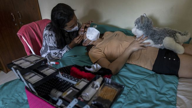 Seorang penyedia jasa salon perawatan kecantikan keliling memasang bulu mata kepada pelanggan di kamar indekos Semarang, Jawa Tengah, Kamis (27/5/2021). [ANTARA FOTO/Aji Styawan]