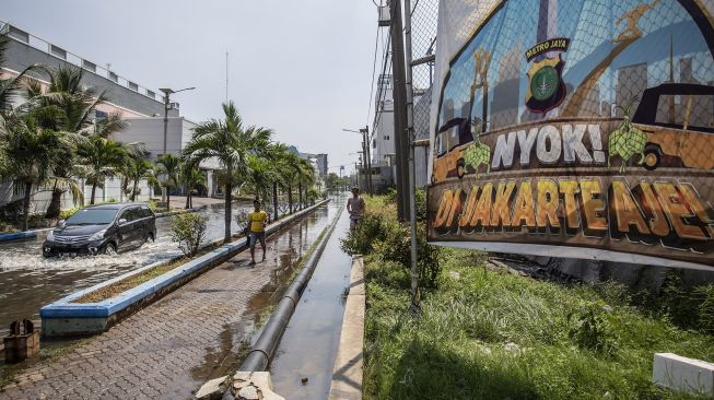 Warga berjalan melintasi banjir rob di kawasan Pelabuhan Perikanan Muara Baru, Jakarta, Jumat (28/5/2021).  ANTARA FOTO/Dhemas Reviyanto
