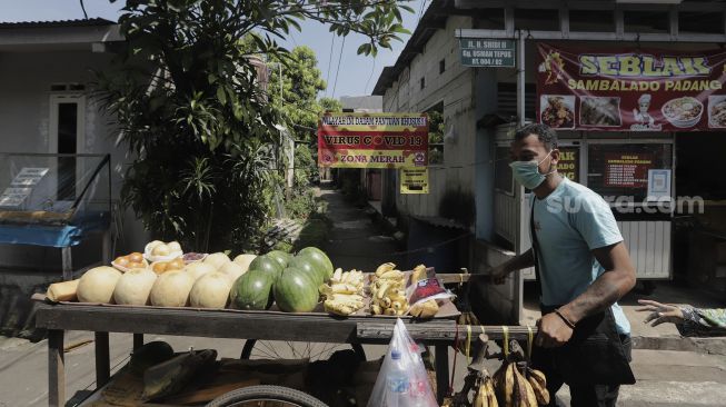 Pedagang buah keliling berjalan di depan Gang Usman Tepos, RT 004 RW 002 Kelurahan Srengseng Sawah, Jagakarsa, Jakarta Selatan, Jumat (28/5/2021). [Suara.com/Angga Budhiyanto]