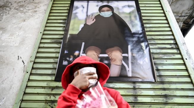 Seorang bocah duduk di depan karya foto saat pameran fotografi bertajuk Meredah COVID-19 di kawasan Pasar Lama, Tangerang, Banten, Minggu (30/5/2021). 
