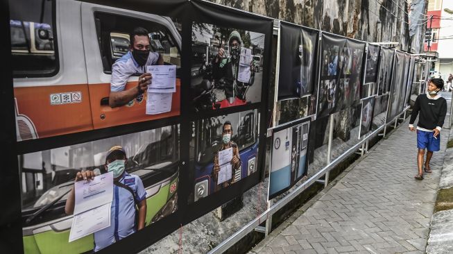 Warga melintas di depan karya foto saat pameran fotografi bertajuk Meredah COVID-19 di kawasan Pasar Lama, Tangerang, Banten, Minggu (30/5/2021).  ANTARA FOTO/Muhammad Adimaja
