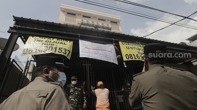 Petugas memasang spanduk tanda penyegelan tempat usaha penginapan Hotel Wisma Prima di Mangga Besar, Taman Sari, Jakarta Barat, Senin (31/5/2021). [Suara.com/Angga Budhiyanto]