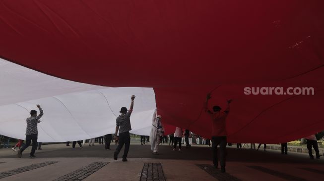 Massa menyemprtokan cairan disinfektan saat pengibaran bendera merah putih raksasa di kawasan Patung Kuda Arjuna Wiwaha, Jakarta, Rabu (2/6/2021). [Suara.com/Angga Budhiyanto]