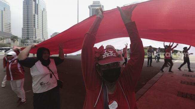 Sejumlah massa mengibarkan bendera merah putih raksasa di kawasan Patung Kuda Arjuna Wiwaha, Jakarta, Rabu (2/6/2021). [Suara.com/Angga Budhiyanto]