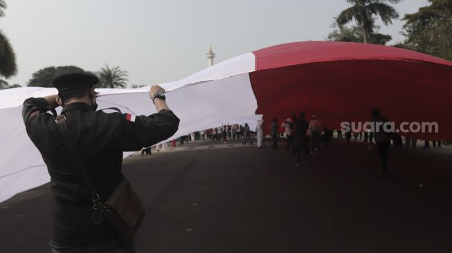 Sejumlah massa mengibarkan bendera merah putih raksasa di kawasan Patung Kuda Arjuna Wiwaha, Jakarta, Rabu (2/6/2021). [Suara.com/Angga Budhiyanto]