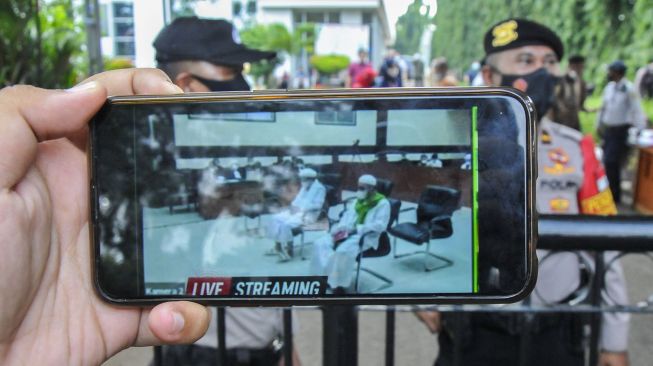 Jurnalis mengamati layar telefon pintar sidang Rizieq Shihab yang beragendakan tuntutan dari Jaksa Penuntut Umum (JPU) di Pengadilan Negeri Jakarta Timur, Kamis (3/6/2021).  ANTARA FOTO