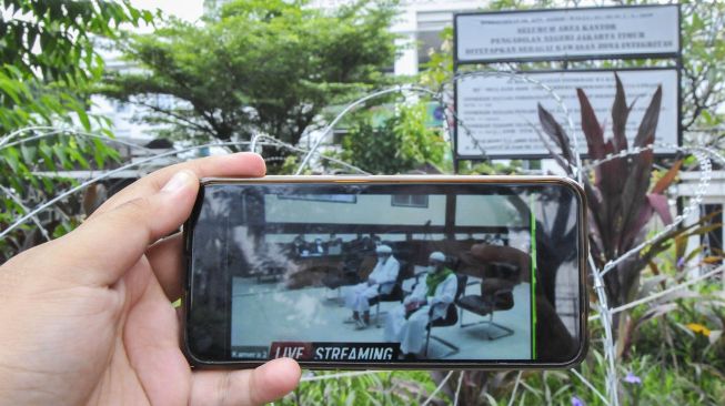 Jurnalis mengamati layar telefon pintar sidang Rizieq Shihab yang beragendakan tuntutan dari Jaksa Penuntut Umum (JPU) di Pengadilan Negeri Jakarta Timur, Kamis (3/6/2021).  ANTARA FOTO