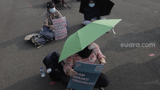 Aktivis lingkungan hidup membawa poster saat melakukan aksi Jeda Untuk Iklim di kawasan Patung Kuda Arjuna Wiwaha, Jakarta, Jumat (4/6/2021). [Suara.com/Angga Budhiyanto]