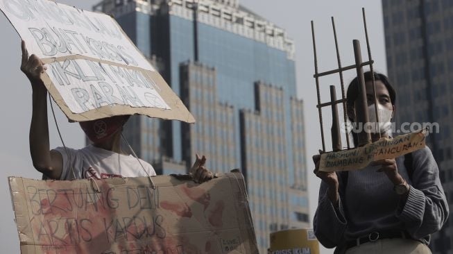 Aktivis lingkungan hidup membawa poster beserta atribut saat melakukan aksi Jeda Untuk Iklim di kawasan Patung Kuda Arjuna Wiwaha, Jakarta, Jumat (4/6/2021). [Suara.com/Angga Budhiyanto]