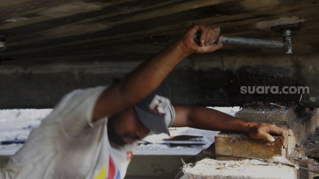 Seorang pekerja memperbaiki kapal di sebuah galangan kapal di kawasan Muara Angke, Jakarta Utara, Jumat (4/6/2021). [Suara.com/Dian Latifah] 