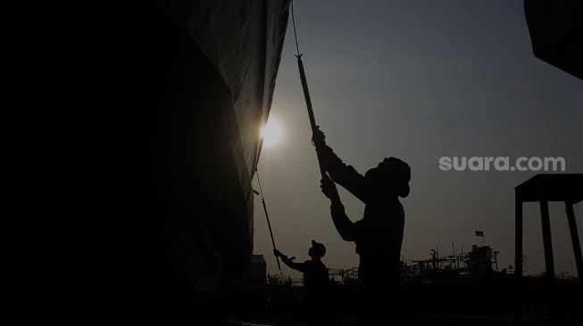 Siluet pekerja memperbaiki kapal di sebuah galangan kapal di kawasan Muara Angke, Jakarta Utara, Jumat (4/6/2021). [Suara.com/Dian Latifah] 