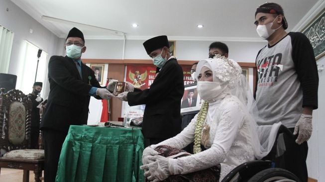 Penghulu menyerahkan buku nikah kepada pengantin saat acara Nikah Gratis di KUA Sewon, Bantul, DI Yogyakarta, Selasa (8/6/2021). ANTARA FOTO/Hendra Nurdiyansyah
