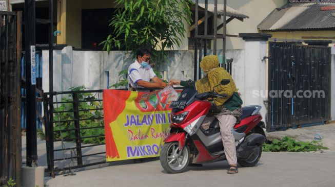 Pengendara bertbicara dengan satpam Perumahan Villa Mutiara Gading 1, Desa Asih, Kecamatan Tarumajaya, Kabupaten Bekasi, Rabu (9/6/2021). [Suara.com/Dian Latifah]