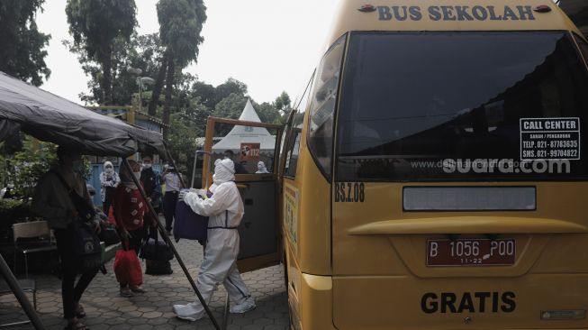 Petugas membantu membawa barang bawaan pasien terkonfirmasi COVID-19 ke dalam bus sekolah yang dioperasikan Dinas Perhubungan DKI Jakarta di Puskesmas Kecamatan Pasar Minggu, Jakarta, Jumat (11/6/2021). [Suara.com/Angga Budhiyanto]