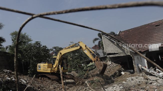 Petugas dibantu alat berat membersihkan puing-puing reruntuhan rumah yang tertimpa tanah longsor di di Perumahan Nerada Estate Ciputat, Tangerang Selatan, Banten, Sabtu (12/6/2021). [Suara.com/Angga Budhiyanto]