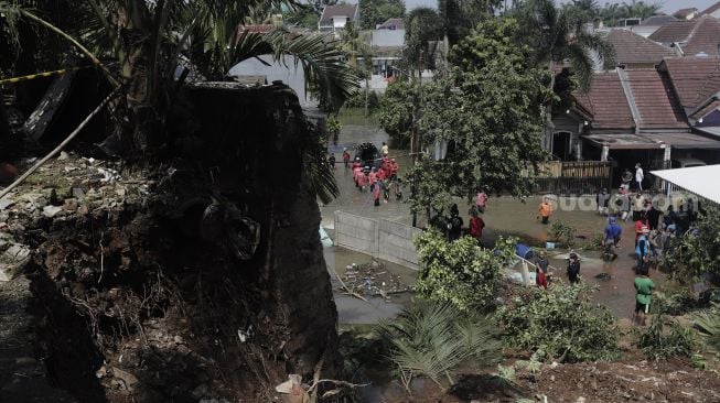 Warga memantau arus air yang masuk dan menyebabkan banjir akibat jebolnya tanggul usai tertimpa tanah longsor di Perumahan Nerada Estate Ciputat, Tangerang Selatan, Banten, Sabtu (12/6/2021). [Suara.com/Angga Budhiyanto]