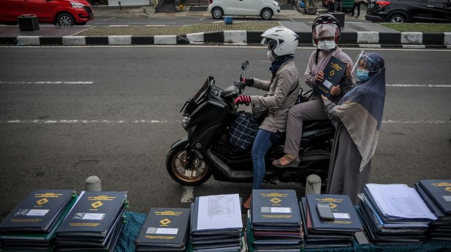 Seorang guru memberikan rapor kepada orang tua siswa saat penerimaan rapor dengan layanan tanpa turun di SD Darul Hikam, Bandung, Jawa Barat, Selasa (15/6/2021).  ANTARA FOTO/Raisan Al Farisi