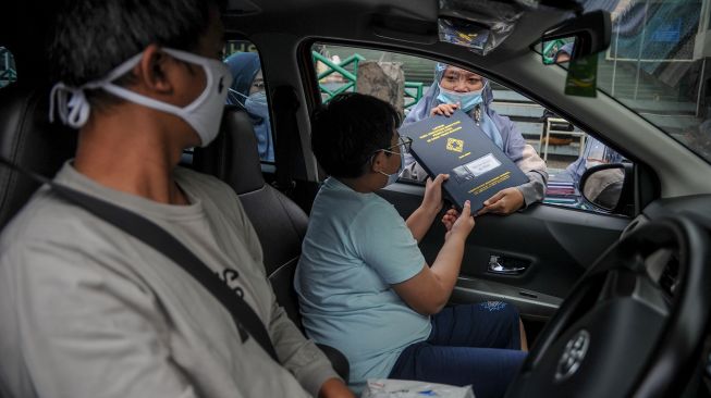 Seorang guru memberikan rapor kepada orang tua siswa saat penerimaan rapor dengan layanan tanpa turun di SD Darul Hikam, Bandung, Jawa Barat, Selasa (15/6/2021).  ANTARA FOTO/Raisan Al Farisi