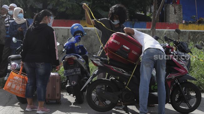 Pekerja Migran Indonesia (PMI) menaikkan barang bawaan ke atas motor usai menjalani isolasi di Rumah Sakit Darurat COVID-19 (RSDC) Wisma Atlet Pademangan, Jakarta, Selasa (15/6/2021). [Suara.com/Angga Budhiyanto]