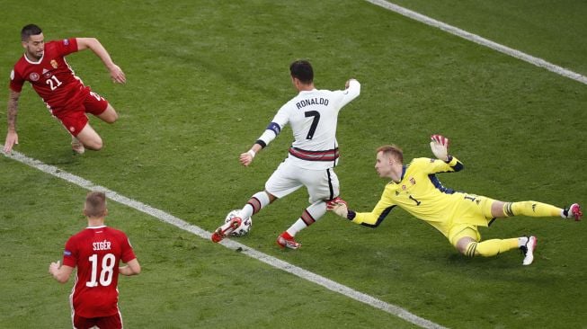 Pemain depan Portugal Cristiano Ronaldo mencetak gol ketiga timnya melewati kiper Hongaria Peter Gulacsi (kanan) selama pertandingan sepak bola Grup F EURO 2020 antara Hungaria melawan Portugal di Puskas Arena di Budapest , Rabu (16/6/2021) dini hari WIB. Laszlo Balogh / AFP / POOL