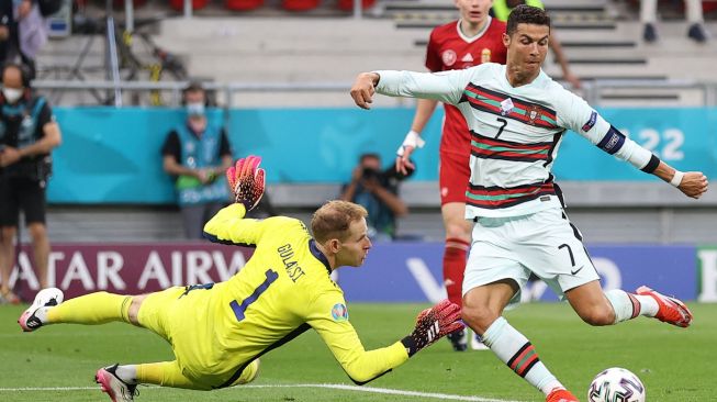 Pemain depan Portugal Cristiano Ronaldo mencetak gol ketiga timnya melewati kiper Hongaria Peter Gulacsi (kanan) selama pertandingan sepak bola Grup F EURO 2020 antara Hungaria melawan Portugal di Puskas Arena di Budapest , Rabu (16/6/2021) dini hari WIB. Laszlo Balogh / AFP / POOL