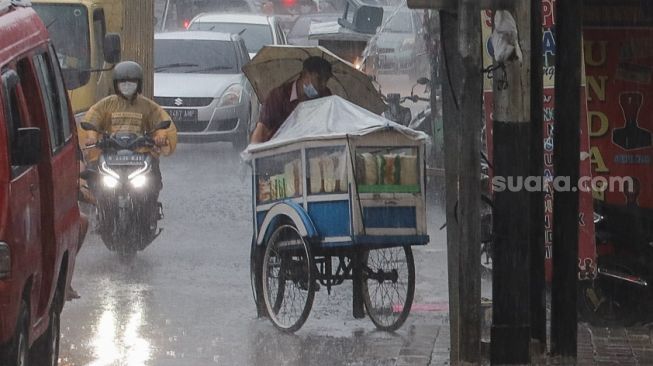 Seorang pedagang menerobos derasnya hujan di kawasan Pinang Ranti, Jakarta Timur, Jumat (18/6/2021). [Suara.com/Alfian Winanto]