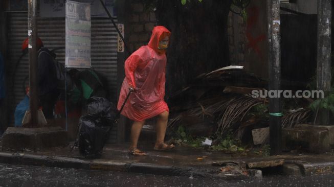 Warga beraktivitas dengan mengenakan jas hujan saat hujan deras di kawasan Pinang Ranti, Jakarta Timur, Jumat (18/6/2021). [Suara.com/Alfian Winanto]
