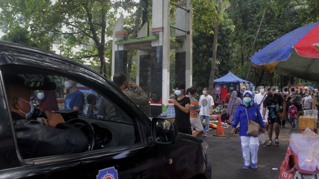 Petugas memberi imbauan kepada sejumlah warga yang memadati kawasan Hutan Kota untuk menerapkan protokol kesehatan di Bekasi, Jawa Barat, Minggu (20/6/2021). [Suara.com/Dian Latifah] 