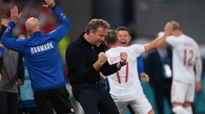 Pelatih Denmark Kasper Hjulmand bersama para staf dan pemain merayakan kepastian timnya lolos 16 besar Euro 2020 usai menang 4-1 atas Rusia, Selasa (22/6/2021) dini hari WIB. (Foto: Stuart FRANKLIN/AFP)