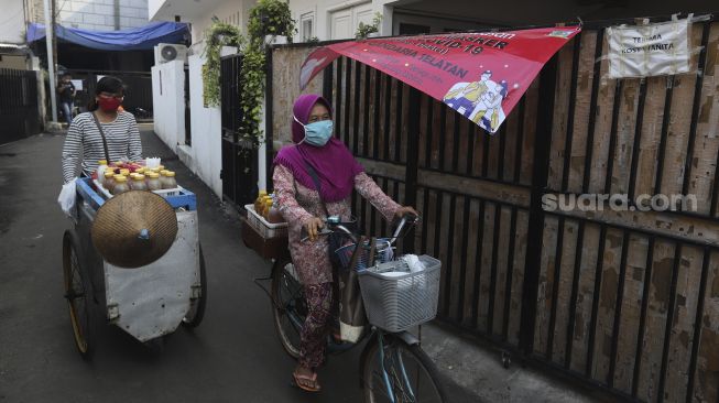 Pedagang jamu keliling melintas di zona merah COVID-19 RT 006 RW 01, Gandaria Selatan, Cilandak, Jakarta, Selasa (22/6/2021). [Suara.com/Angga Budhiyanto]