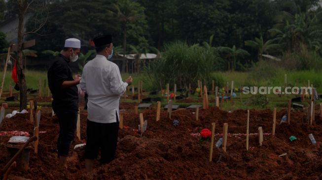 Keluarga berdoa di makam jenazah pasien covid-19 di TPU Padurenan, Mustika Jaya, Bekasi, Rabu (23/6/2021). [Suara.com/Dian Latifah]   