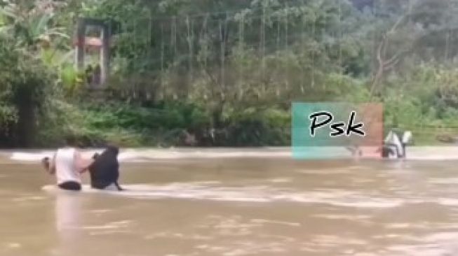 Seorang perempuan berhijab viral di media sosial. Bergelantungan dan meniti tali jembatan gantung. Menyeberangi sungai di Kabupaten Mamasa, Sulbar [SuaraSulsel.id / Instagram peristiwa_sekitar_kita]