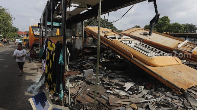 Seorang warga berjalan di dekat potongan bus Transjakarta di Terminal Pulogadung, Jakarta, Kamis (24/6/2021). [Suara.com/Angga Budhiyanto]