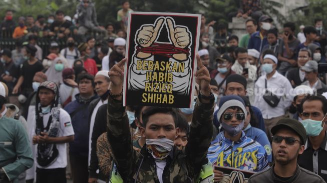 Massa pendukung Rizieq Shihab membawa poster saat tertahan oleh blokade polisi di kawasan I Gusti Ngurah Rai, Jakarta, Kamis (24/6/2021). [Suara.com/Angga Budhiyanto]