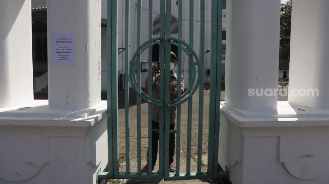 Petugas keamanan menutup gerbang saat peniadaan sholat Jumat di Masjid Cut Meutia, Jakarta, Jumat (25/6/2021). [Suara.com/Angga Budhiyanto]