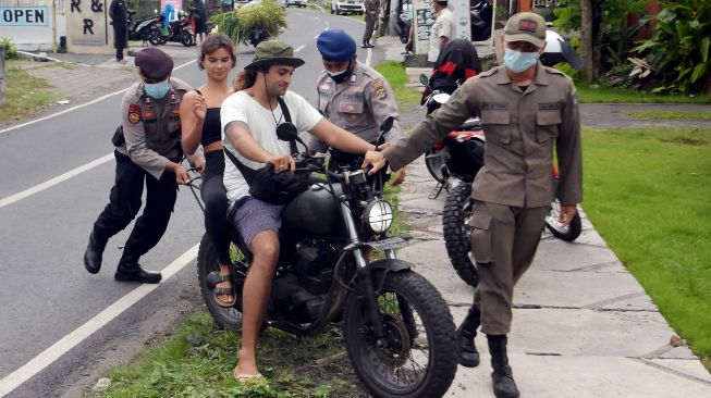 Anggota Polisi dan Satpol PP Kabupaten Badung menghentikan warga negara asing (WNA) yang melanggar protokol kesehatan saat operasi penertiban prokes dalam Pemberlakuan Pembatasan Kegiatan Masyarakat (PPKM) skala mikro di Desa Canggu, Badung, Bali, Jumat (25/6/2021). ANTARA FOTO/Nyoman Hendra Wibowo