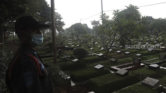 Petugas keamanan berjaga di Tempat Pemakaman Umum (TPU) Karet Bivak, Jakarta, Minggu (27/6/2021). [Suara.com/Angga Budhiyanto]