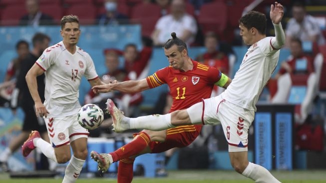 Pemain depan Wales Gareth Bale (tengah) memainkan bola di bawah tekanan dari bek Denmark Andreas Christensen (kanan) dan bek Denmark Jens Stryger Larsen (kiri) selama pertandingan sepak bola babak 16 besar UEFA EURO 2020 antara Wales dan Denmark di Johan Cruyff Arena, Amsterdam, pada (26/6/2021). [Kenzo Tribouillard / POOL / AFP]