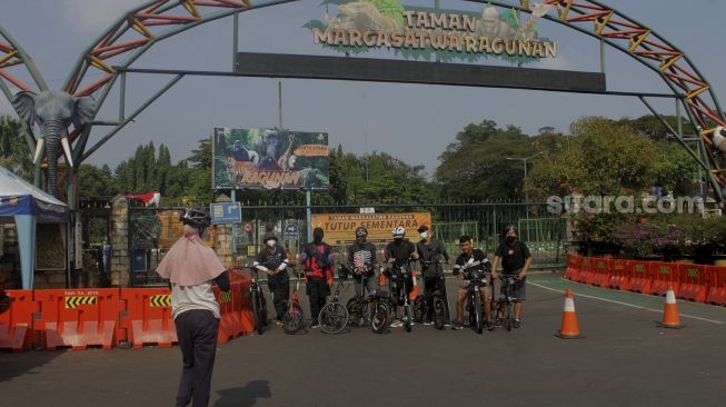 Sejumlah pesepeda berfoto di depan gerbang utama Taman Margasatwa Ragunan, Jakarta, Minggu (27/6/2021). [Suara.com/Dian Latifah]