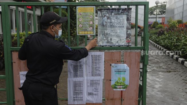 Petugas keamanan menutup pintu masuk Tempat Pemakaman Umum (TPU) Karet Bivak, Jakarta, Minggu (27/6/2021). [Suara.com/Angga Budhiyanto]