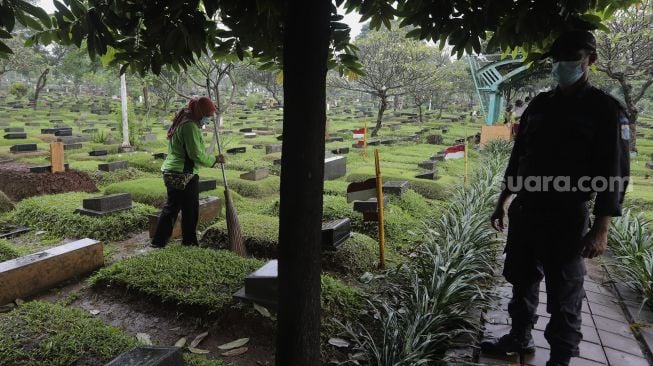 Petugas membersihkan makam di Tempat Pemakaman Umum (TPU) Karet Bivak, Jakarta, Minggu (27/6/2021). [Suara.com/Angga Budhiyanto]