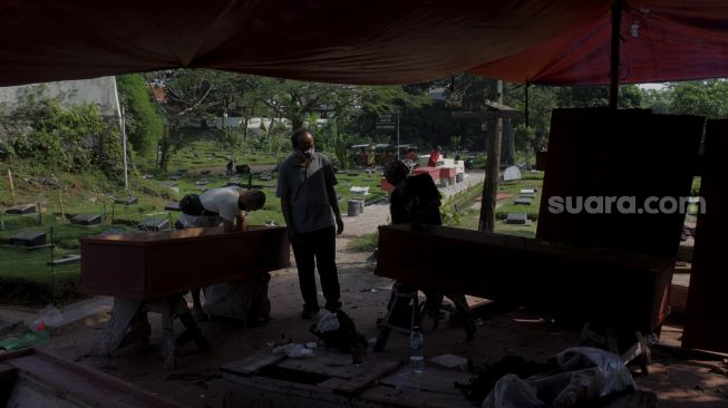 Pekerja menyelesaikan pembuatan peti mati di Yayasan Sahabat Duka, TPU Pondok Kelapa, Jakarta, Selasa (29/6/2021). [Suara.com/Dian Latifah]