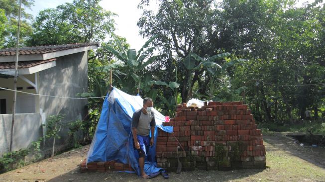 Seorang warga terkonfirmasi positif COVID-19 berada di sekitar tenda terpal untuk menjalani isolasi mandiri di desa Lohbener, Indramayu, Jawa Barat, Rabu (30/6/2021).  ANTARA FOTO/Dedhez Anggara