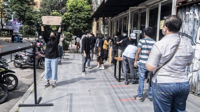 Seorang barista membawa papan pengumuman pembagian kopi gratis bagi masyarakat yang sudah vaksin COVID-19 di kawasan Blok M, Jakarta, Rabu (30/6/2021). ANTARA FOTO/Muhammad Adimaja