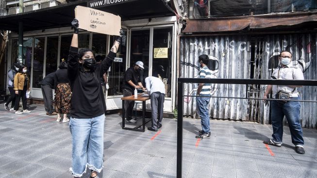 Seorang barista membawa papan pengumuman pembagian kopi gratis bagi masyarakat yang sudah vaksin COVID-19 di kawasan Blok M, Jakarta, Rabu (30/6/2021). ANTARA FOTO/Muhammad Adimaja